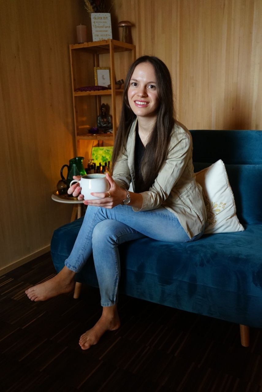 Kim lächelt mit einer Tasse auf dem Sofa